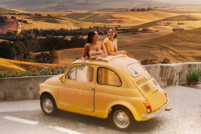 Young women driving a yellow Fiat 500 through the Tuscan countryside